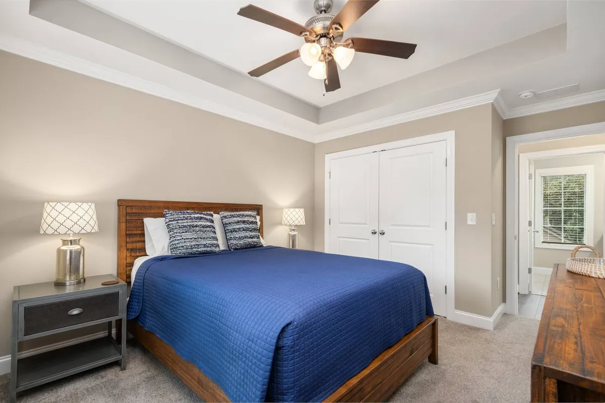 A bright bedroom with a stylish blue quilt on the bed, flanked by nightstands topped with matching lamps. A sturdy wooden dresser sits nearby, and sunlight streams in, enhancing the room's peaceful vibe. The overall setup suggests comfortable, restful accommodations.
