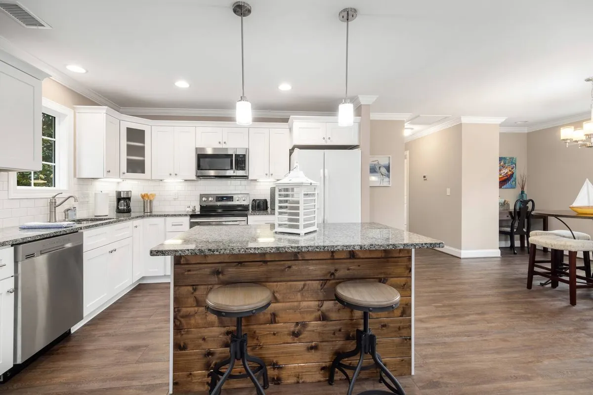 A modern kitchen scene featuring a granite countertop, wooden bar stools, stainless steel appliances, and crisp white cabinetry. The warm natural light enhances the sustainable and welcoming atmosphere.