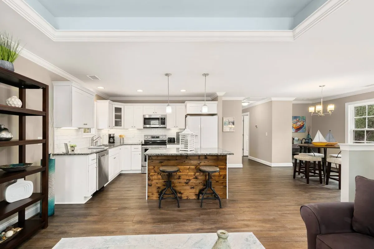 This interior view shows a kitchen island with stools, an open layout, and a dining area visible beyond. The space is styled for comfort and togetherness, inviting group gatherings and socializing, with clear sightlines between gathering spots.