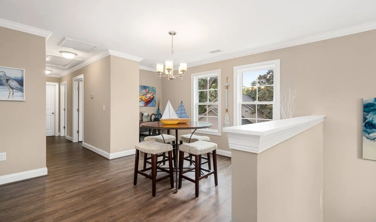A bright, welcoming interior shot of the dining area with bar stools, a round table, and decorative artwork. Sunlight streams through the windows, suggesting a lively yet comfortable space to gather before heading out or to unwind after enjoying Charleston's nightlife.