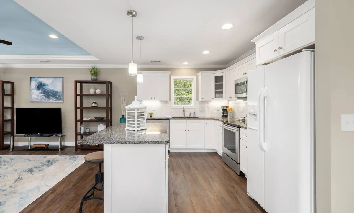 This image presents a spacious kitchen with a granite countertop, island seating, white cabinetry, and a window with a green view. The area exudes a bright, convivial mood, perfect for both cooking and gathering.